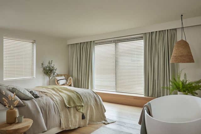 faux wood Venetian blinds fitted to two windows in a bedroom decorated in white and natural wood colours