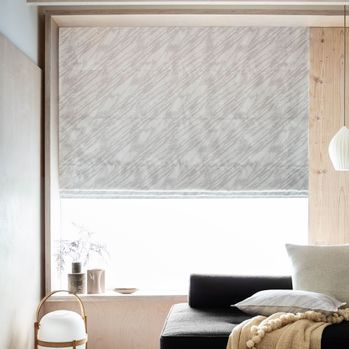 Drift Alabaster grey and white roman blind in large wooden framed living room window with gold and navy accessories