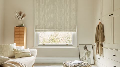 cream coloured roman blind with a white vertical pattern fitted to a window in a white decorated living room