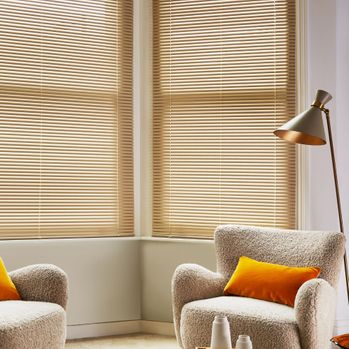 Harvest gold colour metal venetian blind in large living room way window with boucle chair