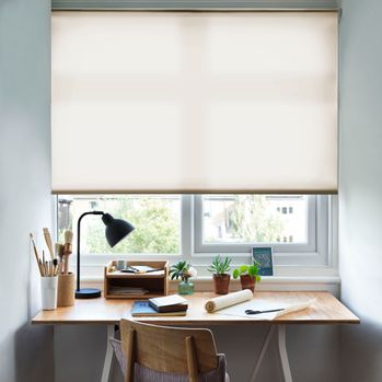 Reber Beige Roller Blind with a desk in front of the window and a lamp on the table and office stationary
