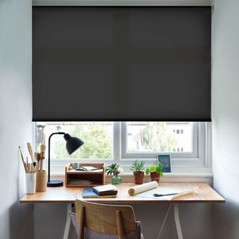 Reber Night Roller Blind with a desk in front of the window and a lamp on the table and office stationary