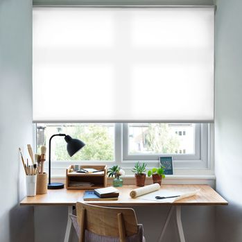 Reber Pure White Roller Blind with a desk in front of the window and a lamp on the table and office stationary