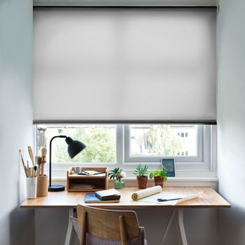 Reber Ash Roller Blind with a desk in front of the window and a lamp on the table and office stationary