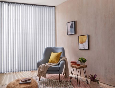 Reber Silver vertical blinds in a living nook with a blue chair in the center with a yellow pillow and pink blanket on it