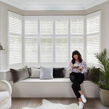 Anna Richardson sat in a white decorated living room with a bay window that has tiered silk white shutters 