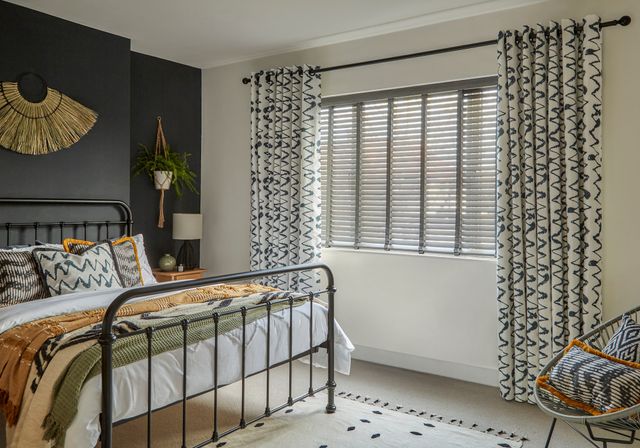 Wood Venetian Mirage Faux Wood Charcoal Blinds paired with Wolfe Smoulder Curtains in a bedroom with a bed on the left side