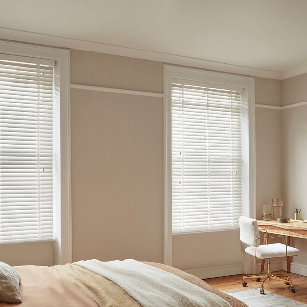 Ellwood Crystal White Wooden Blinds in a cream bedroom with a desk on he right side and a bed on the left. 