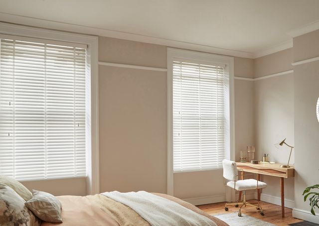 Ellwood Crystal White Wooden Blinds in a cream bedroom with a desk on he right side and a bed on the left. 