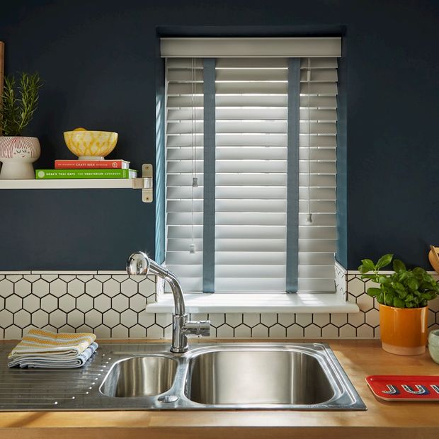 Shades Dove Grey blind in a kitchen with wooden surfaces and a navy wall and a sink in front of the window.