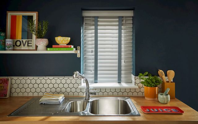 Shades Dove Grey blind in a kitchen with wooden surfaces and a navy wall and a sink in front of the window.