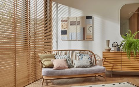 Natural Bamboo Honey blinds on the left side of the room and a wooden rattan chair in the center with art and a mirror on the wall and a wooden cabinet on the right.