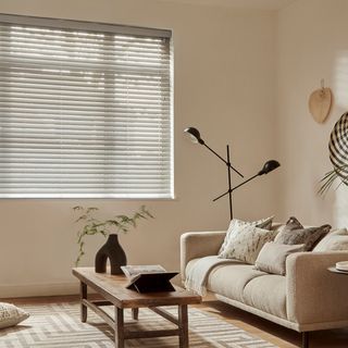 Natural Bamboo blind in Pebble in a living room with wall decorations and a cream sofa on the right side and wooden coffee table in the center. 