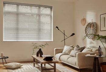 Natural Bamboo blind in Pebble in a living room with wall decorations and a cream sofa on the right side and wooden coffee table in the center. 