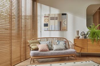 Natural Bamboo blinds on the right side and a wooden double seat chair in the center and a wooden cabinet to the right with a plant on it