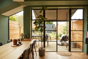 Green walled kitchen with almost a full wall of windows displaying a long garden