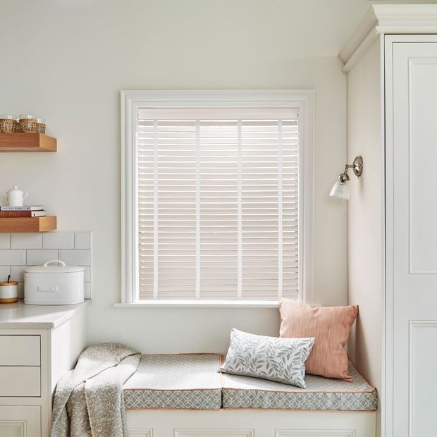 Faux wood venetian bamboo blinds in pearl white on a kitchen window above furnished window ledge