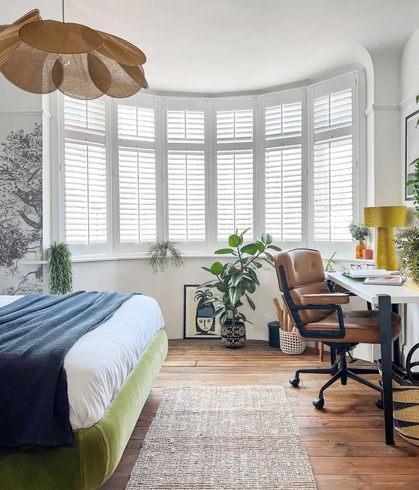 Pure White shutters in a bedroom with the bed to the left and a desk and chair to the right and a rug in the middle