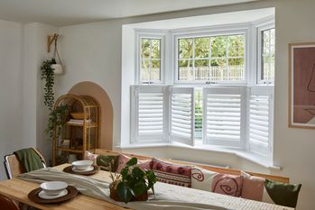 café style white shutters on the bottom half of a dining room window behind a furnished dining table