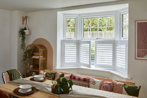 café style white shutters on the bottom half of a dining room window behind a furnished dining table