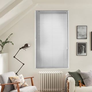 Silver coloured venetian blinds fitted to a tall window in a living room