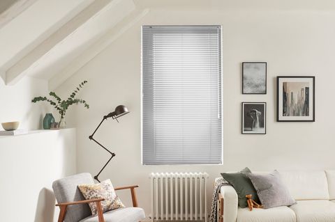 Silver coloured venetian blinds fitted to a tall window in a living room