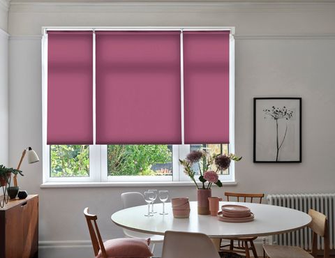 Reber Fuchsia Roller blind in a dining room with a circular table and chairs around it with flowers on the table. 