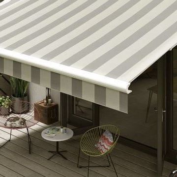 A grey striped awning hanging over patio furniture on a bright day