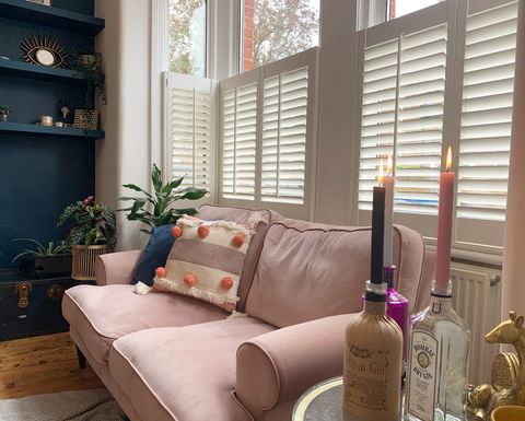 Decorators white cafe shutter in bay window in front of pink sofa in living room