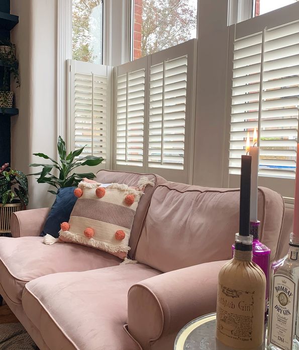 Decorators white cafe shutter in bay window in front of pink sofa in living room