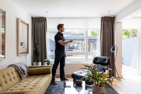 george clarke standing infront of a window holding a remote to control his white roller blinds
