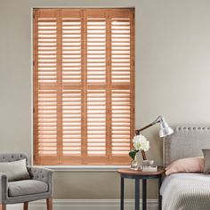 cherry wood shutters in a bedroom inbetween a grey chair and ben on an off white wall