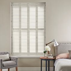 matte white shutters in a bedroom inbetween a grey chair and bed on an off white wall