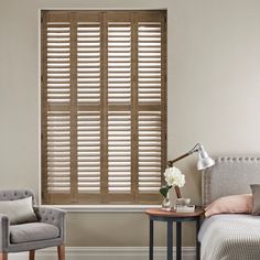 antique oak shutters in a bedroom inbetween a grey chair and bed on an off white wall