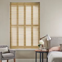 oak coloured shutters in a bedroom inbetween a grey chair and bed on an off white wall