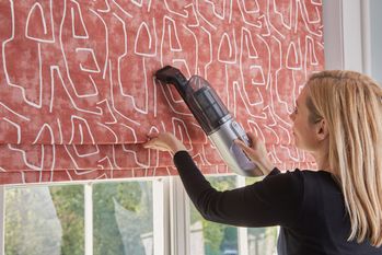 lady with blonde hair using a machine to clean a red roman blind with white patterns on it