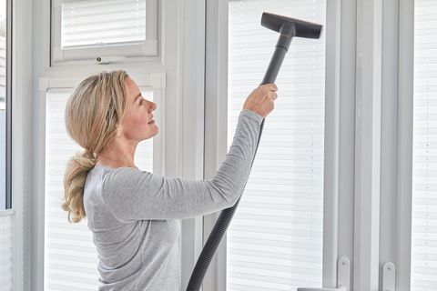 woman cleaning white pleated blinds with vacuum