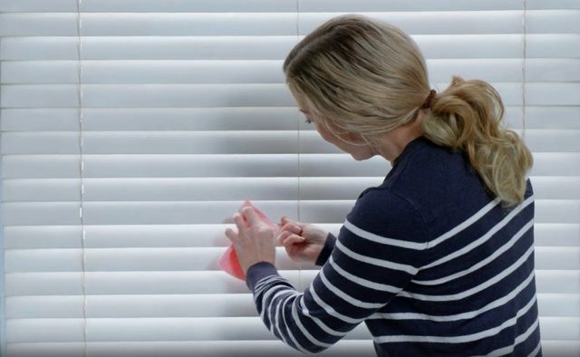 woman cleaning white wooden blinds