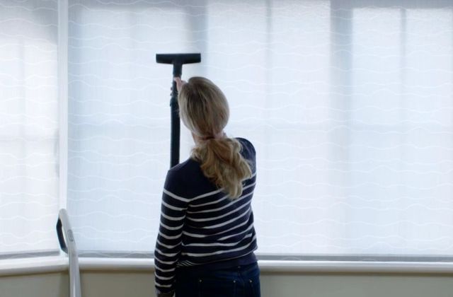 woman vacuuming white roller blind