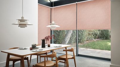Pablo Coral motorised roller blinds in modern kitchen dining area with white and chestnut dining table and chestnut chairs