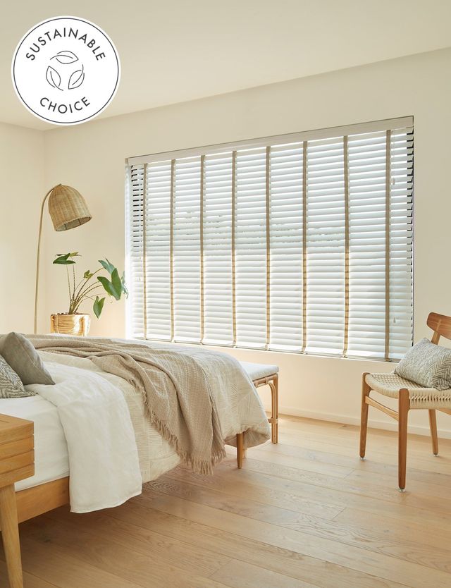 White wooden blinds with brown tape on large window in neutral coloured bedroom