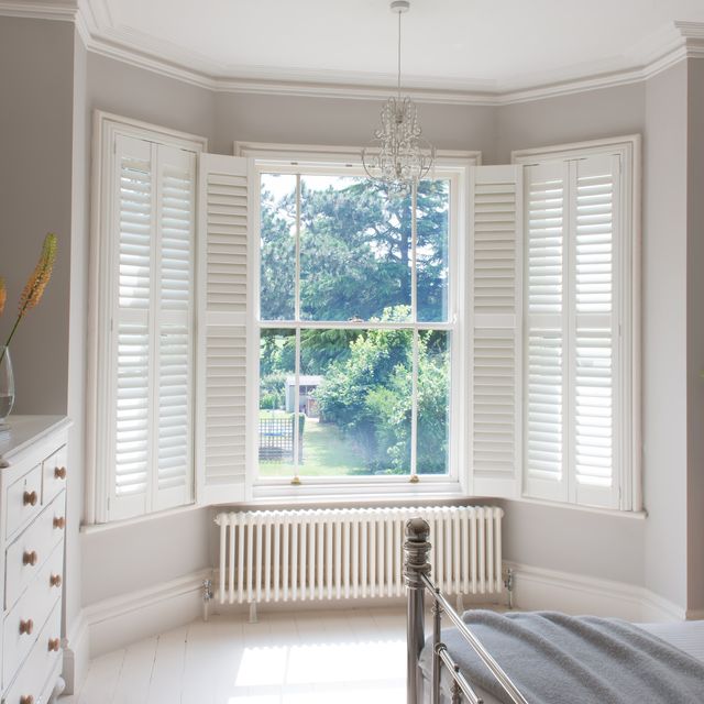 white wooden shutters on a bay window in a spacious bedroom