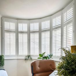 full height pure white shutters on a large curved bay window in a bedroom