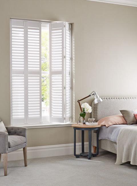 pure white wooden full height shutters on a tall window in a modern bedroom with cosy furnishings