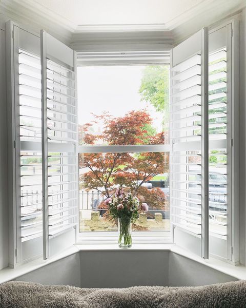 full height open pure white shutters on a bay window in a lounge