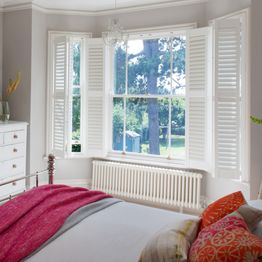 white full height wooden shutters on a bay window in bedroom