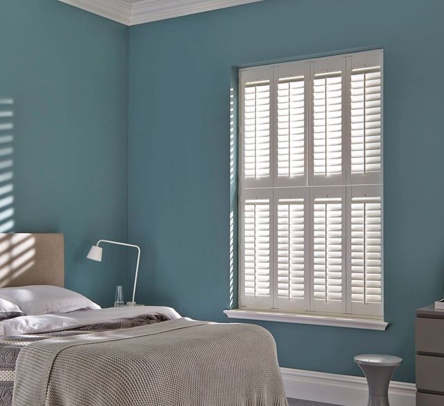 white tier on tier bedroom shutters on window with blue walls and cosy bed