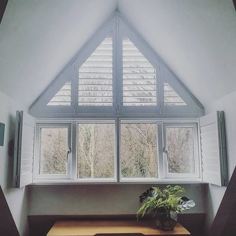 pure white gable end shaped shutters on triangular window in bedroom
