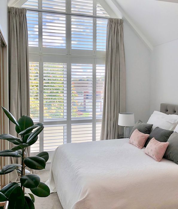 long full height shutters on huge window with triangular shutters on the top in bedroom