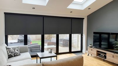 black perfect fit roller blinds on bifold doors in living room with big grey sofa and flatscreen tv